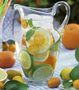 Jug of water with citrus fruit, lemon balm and ice cubes